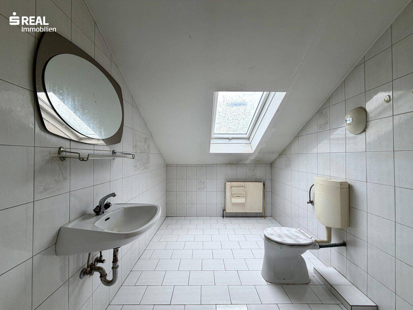 Dachgeschoss-Badezimmer mit Waschbecken, WC, Fliesenboden und Dachfenster.