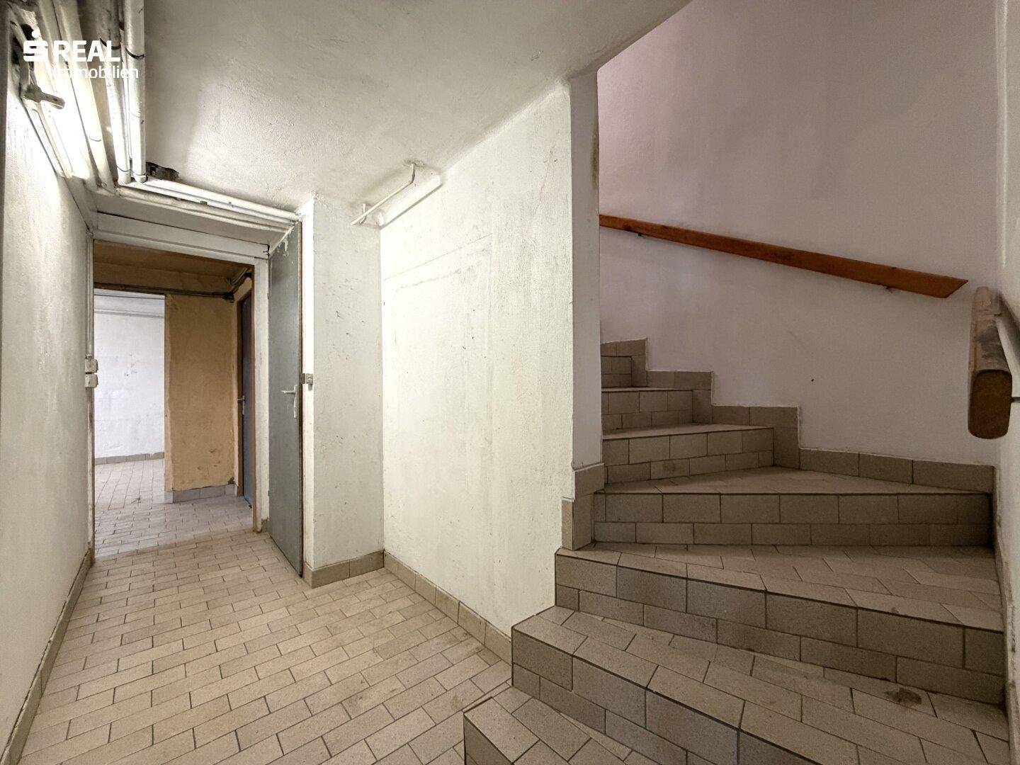 Kellerflur mit Fliesenboden und Treppe zum Obergeschoss, in einfachem Zustand.