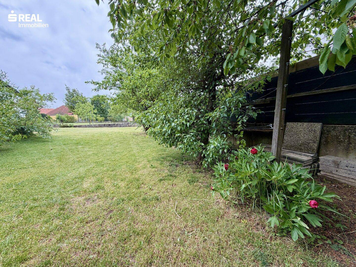 Großer, gepflegter Gartenbereich mit Rasenfläche, Bäumen und blühenden Pflanzen.