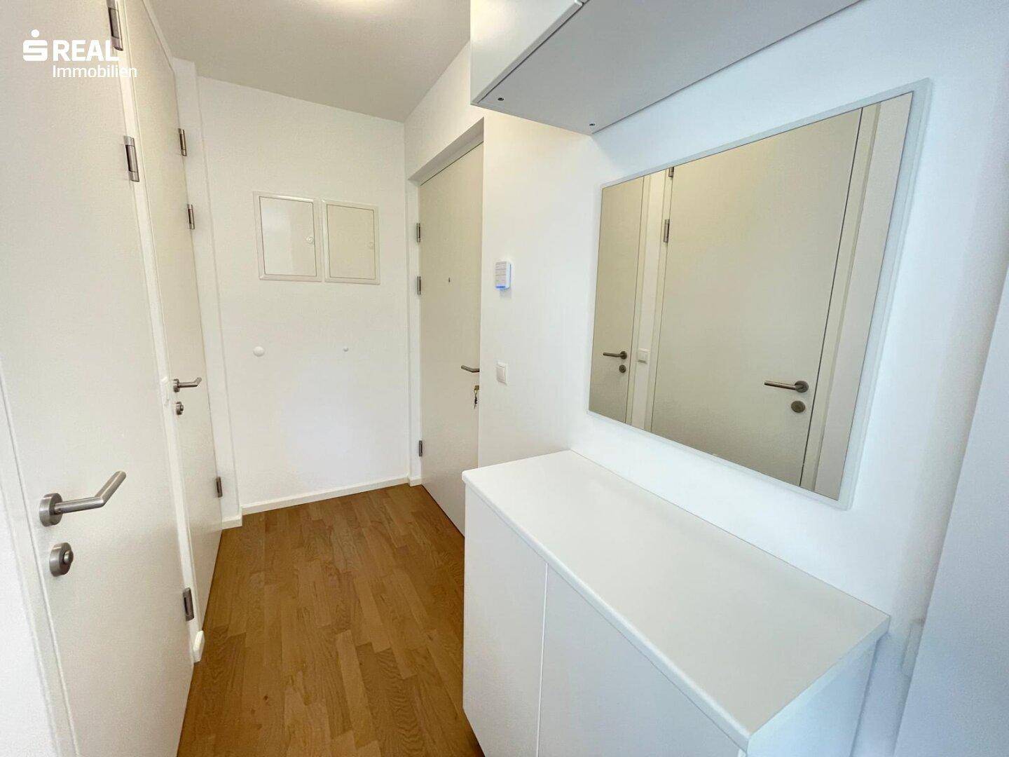 Heller Eingangsbereich mit Holzboden, Garderobe und einem großen Spiegel.