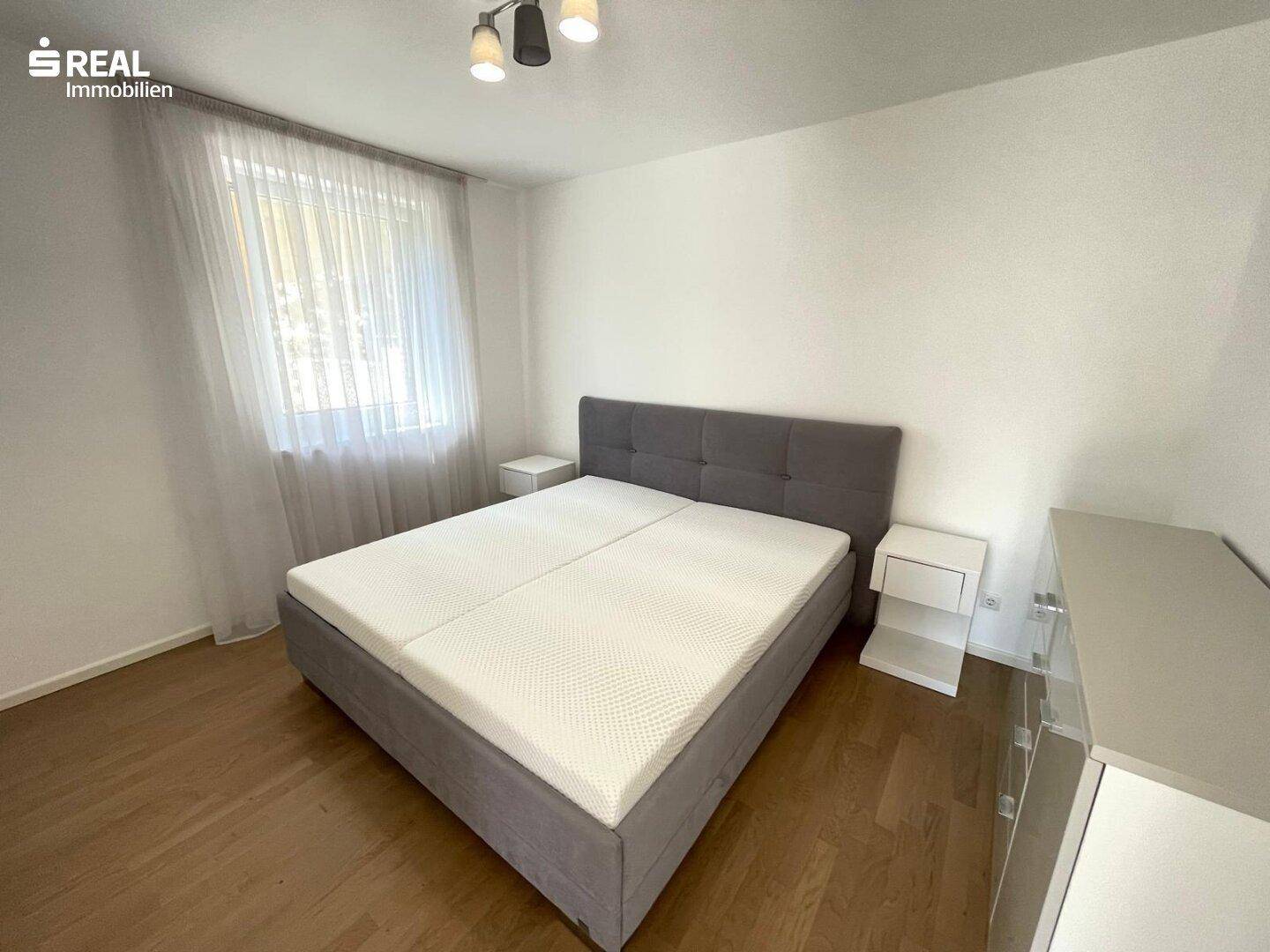 Helles Schlafzimmer mit Doppelbett, Nachttischen und Holzboden, bereit zur Einrichtung.