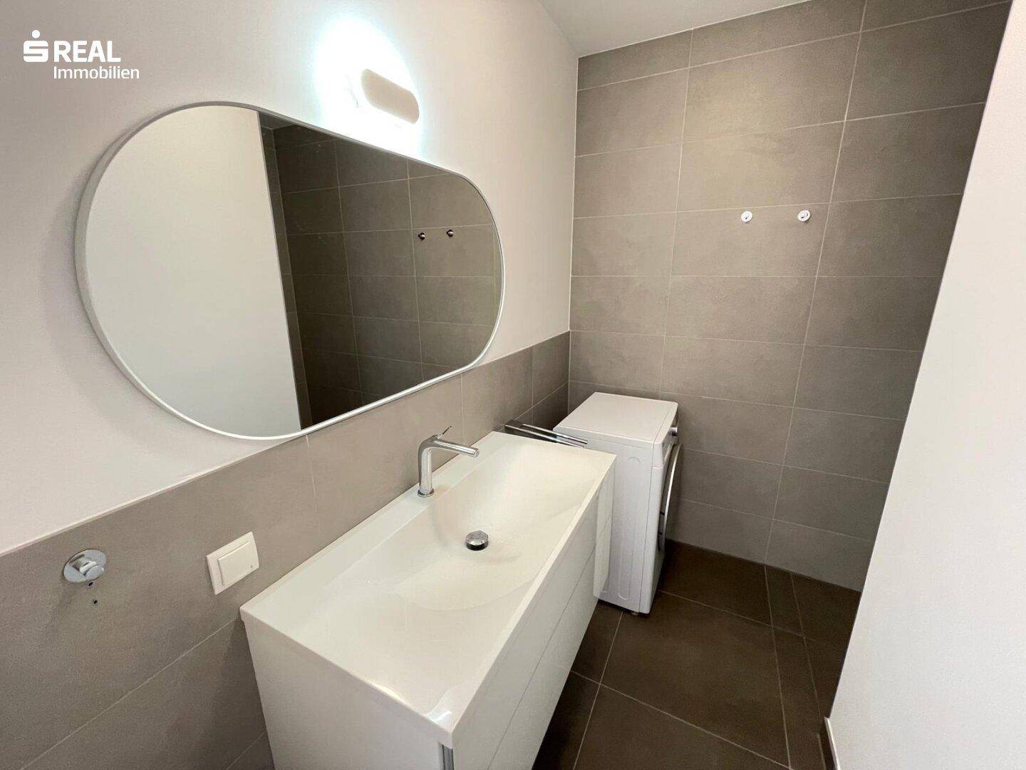 Modernes Badezimmer mit großem Waschbecken, Spiegel und integrierter Waschmaschine.