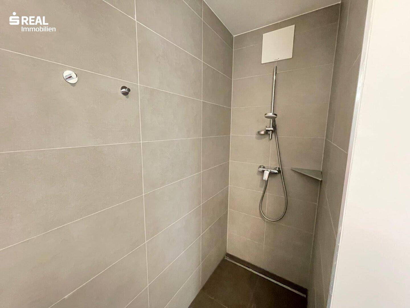Duschbereich im modernen Badezimmer mit grauen Fliesen und einfacher, funktionaler Ausstattung.