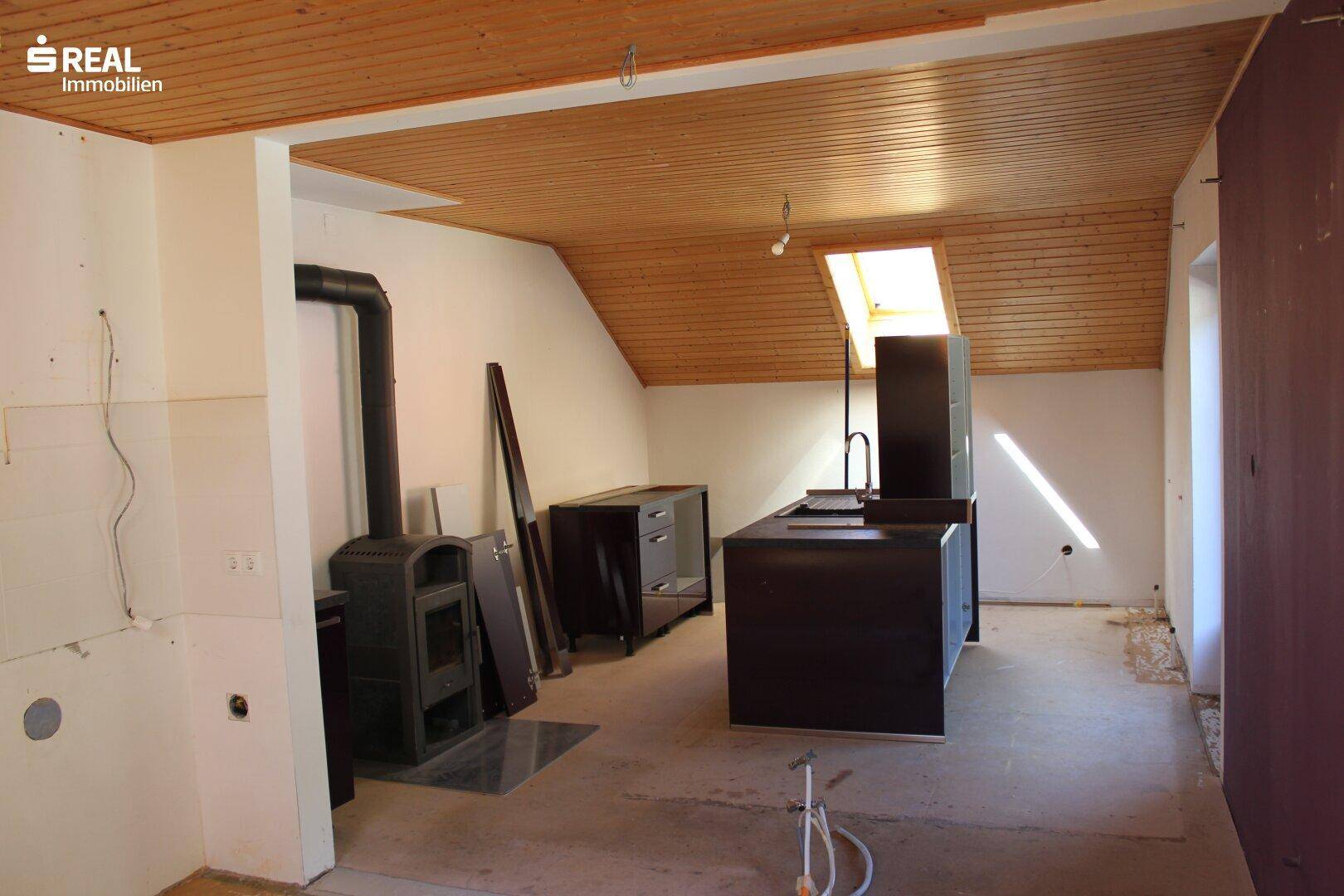 Ausgebauter Dachbodenbereich mit Holzdecke, Dachfenster und Vorbereitung für eine Küche.