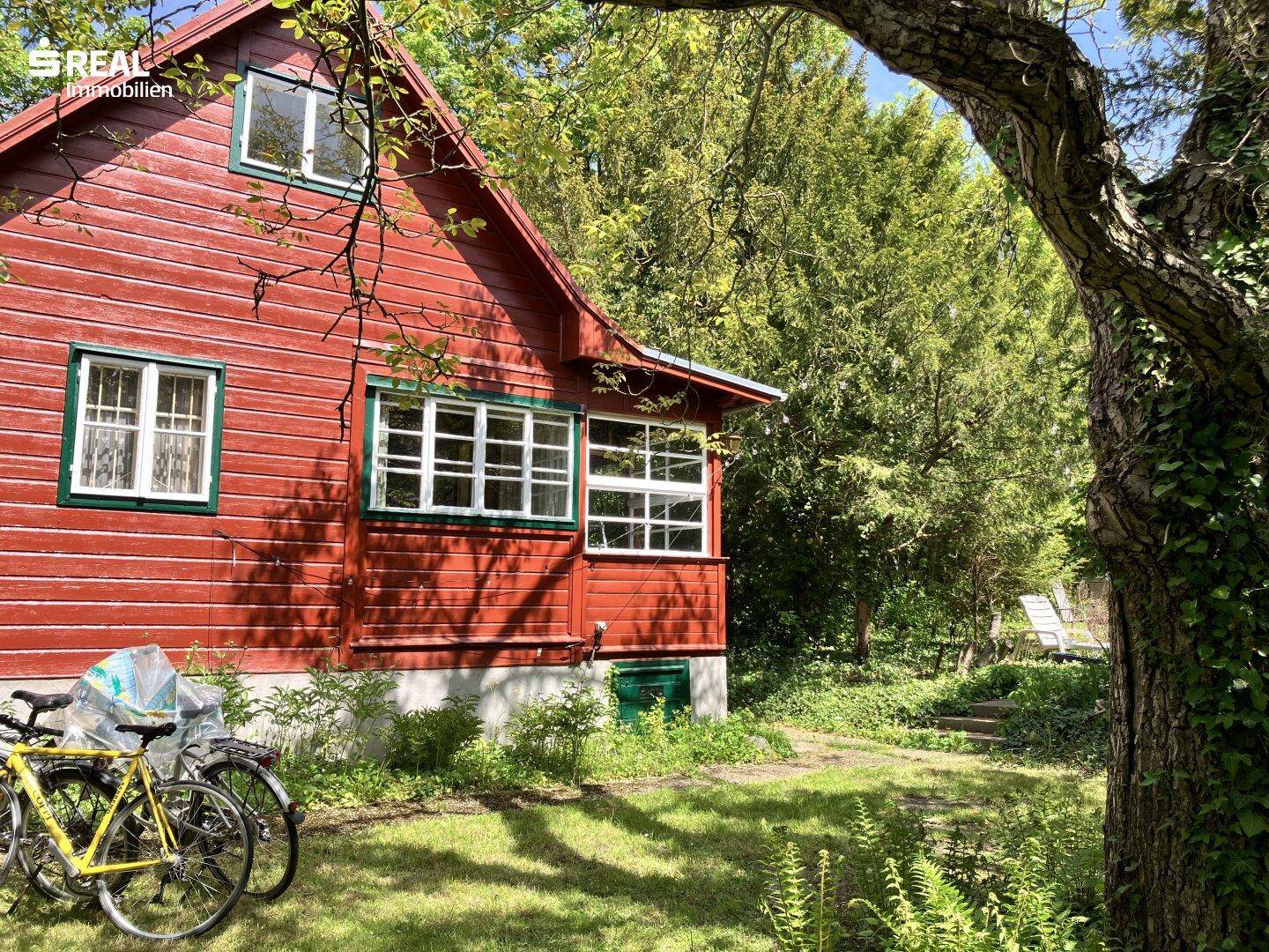 Detailansicht des roten Holzhauses mit weißen Sprossenfenstern und grünen Akzenten im Garten.
