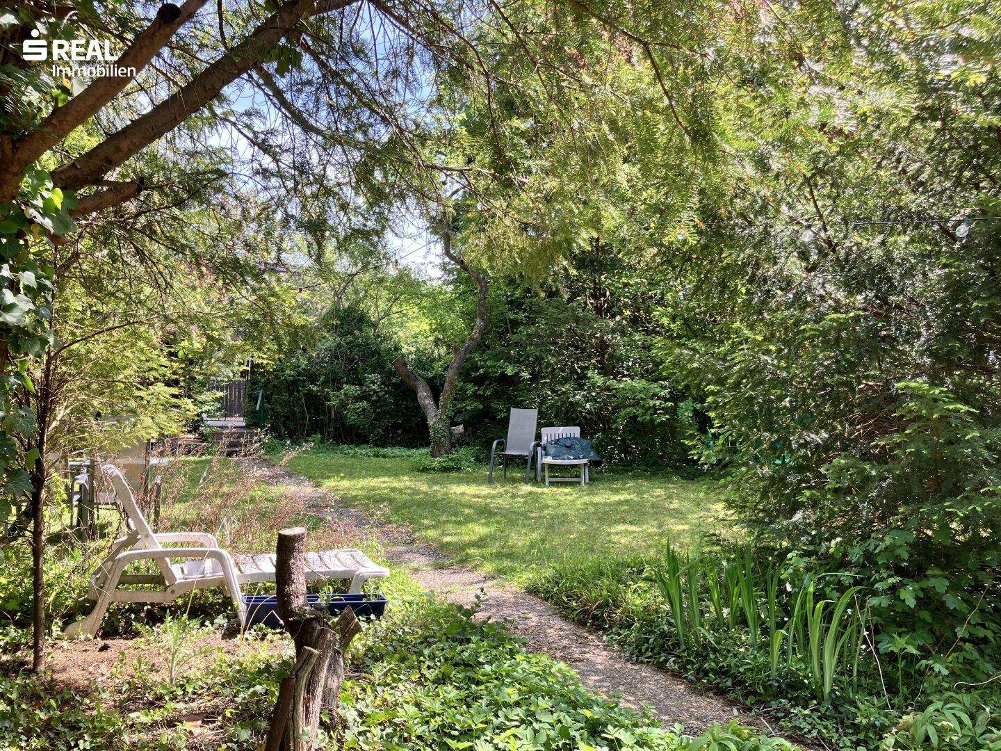 Ruhiger Gartenbereich mit Sitzgelegenheiten und einem gewundenen Pfad, eingebettet in die Natur.