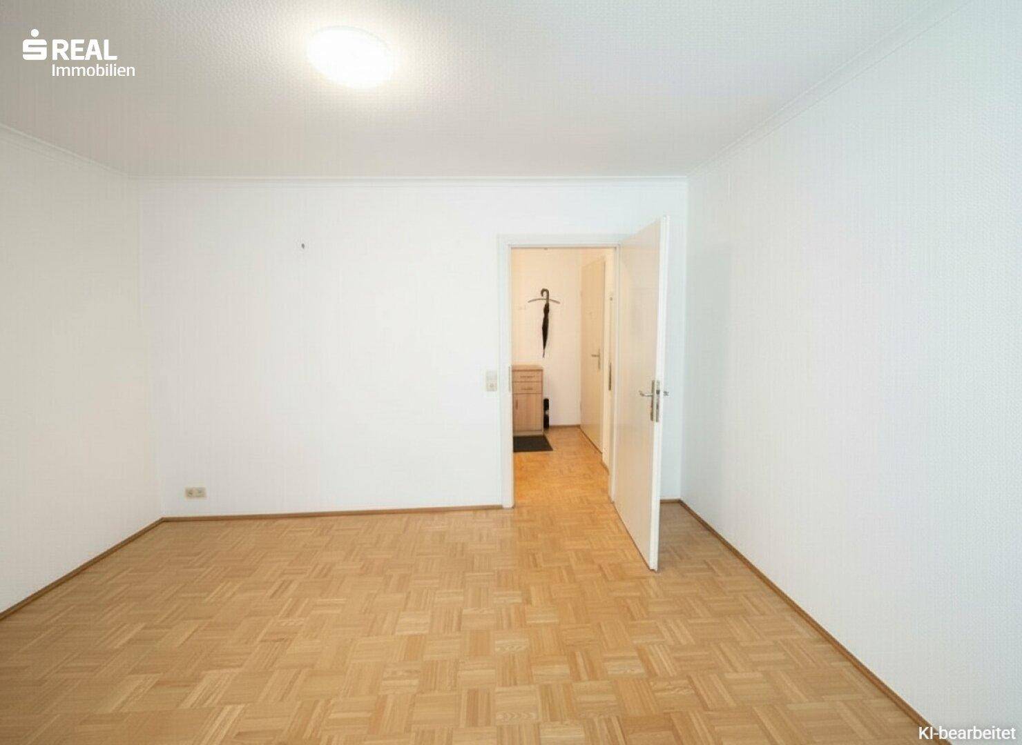 Geräumiges, helles Zimmer mit Parkettboden und Zugang zu einem weiteren Raum.