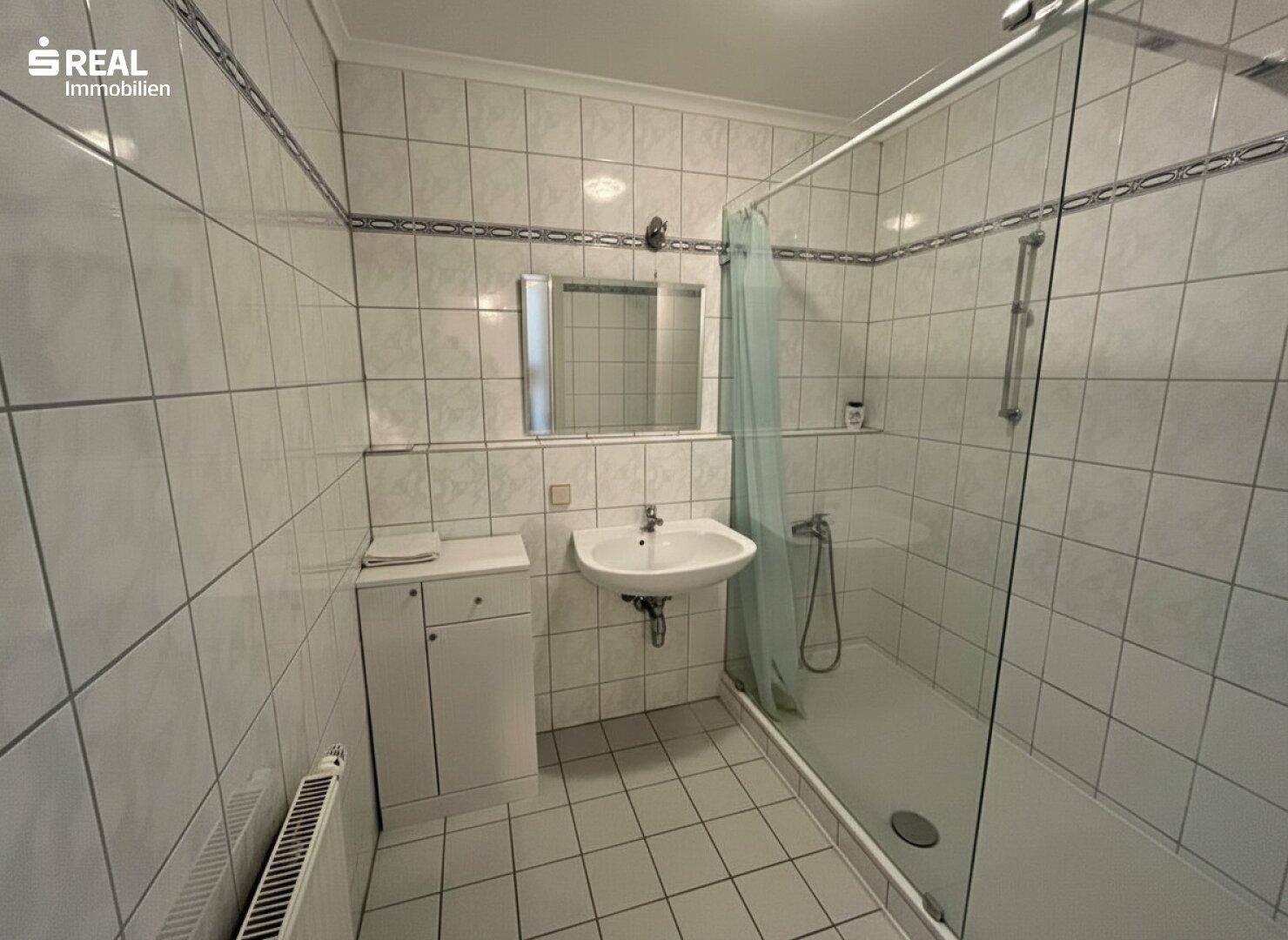 Gefliestes Badezimmer mit Dusche, Waschbecken und Heizkörper, in gutem Zustand.