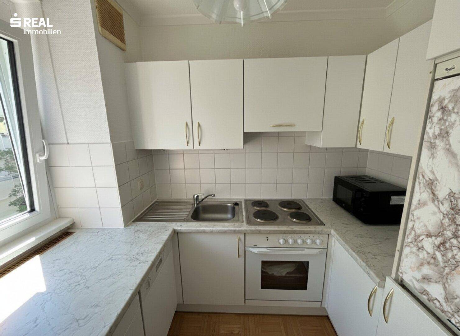Funktionale Küche mit weißen Schränken, Herd und Fenster, bereit zum Kochen.