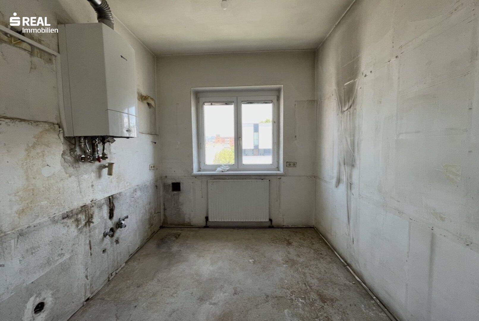 Leerer Raum, wahrscheinlich eine Küche, mit Boiler, Fenster und deutlichen Renovierungsspuren an den Wänden.