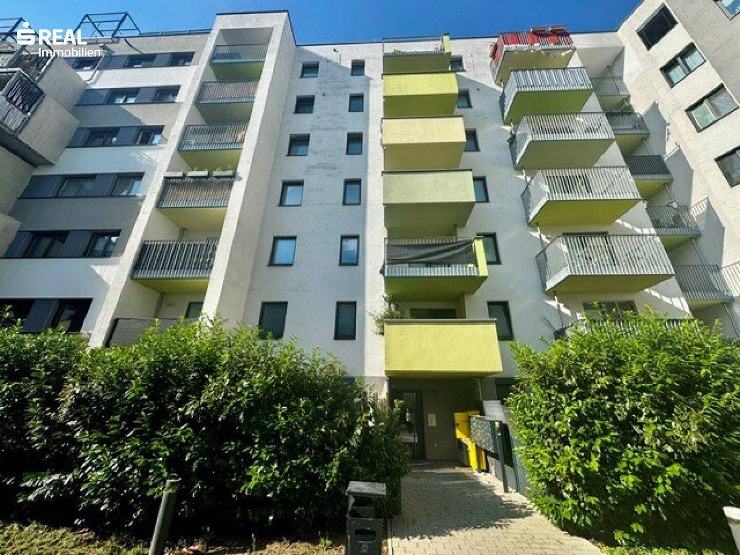 Moderne Wohnhausfassade mit zahlreichen Balkonen und grünen Akzenten in der Architektur.
