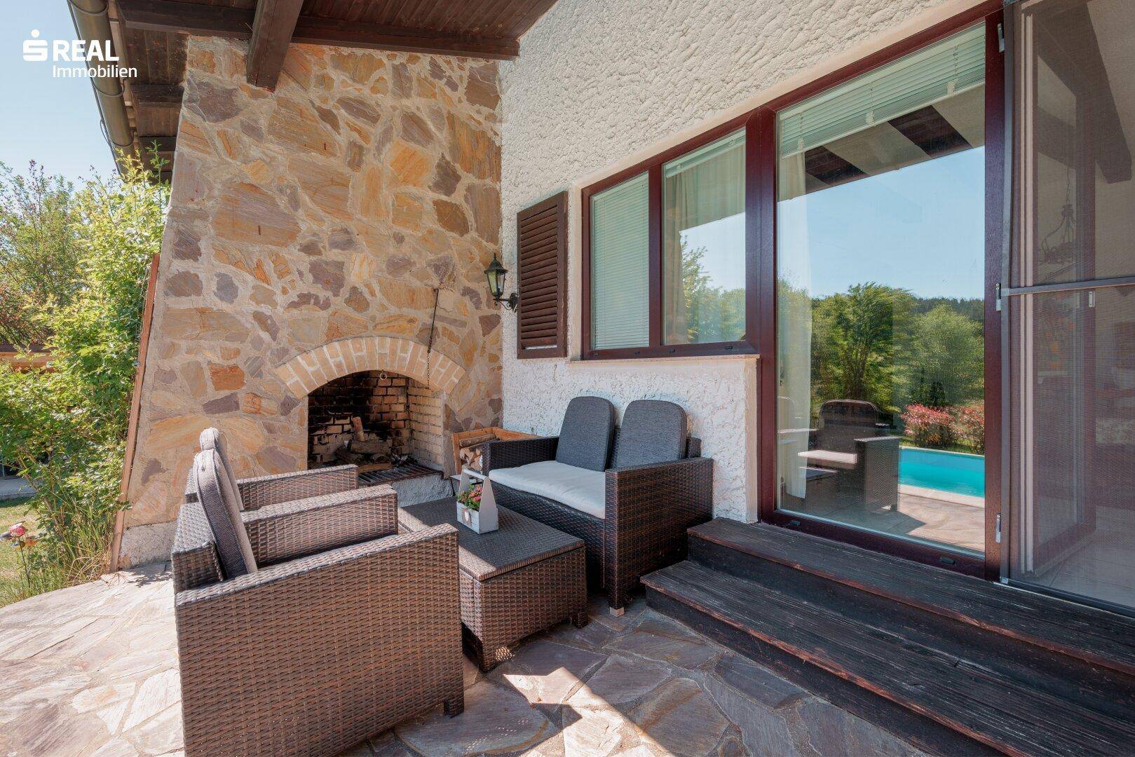 Gemütliche überdachte Terrasse mit Außenkamin und Rattanmöbeln, Blick zum Pool.