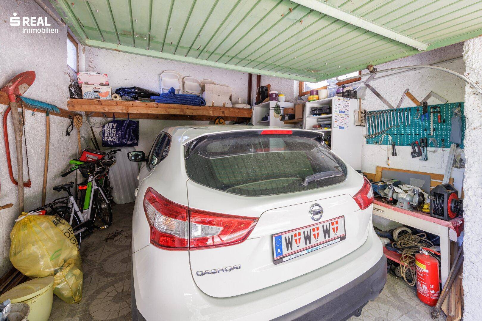 Geräumige Garage mit einem geparkten Auto, Werkzeugen und Abstellmöglichkeiten.