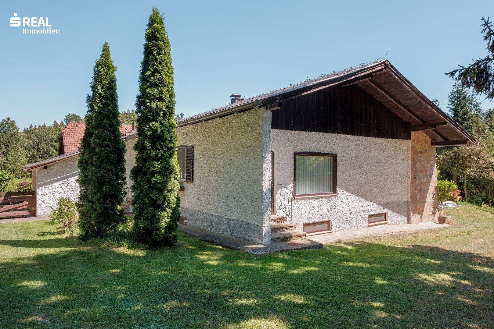 Seitenansicht des Hauses mit weißer Fassade, Holzelementen und weitläufigem Rasenbereich.