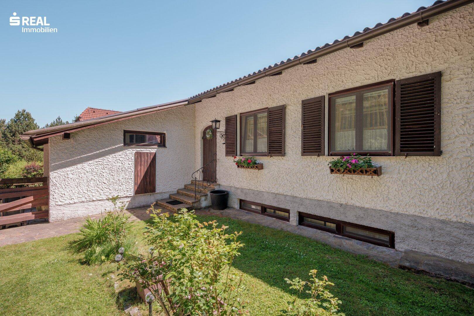 Vorderansicht des Hauses mit weißer Putzfassade, braunen Fensterläden und gepflegtem Vorgarten.