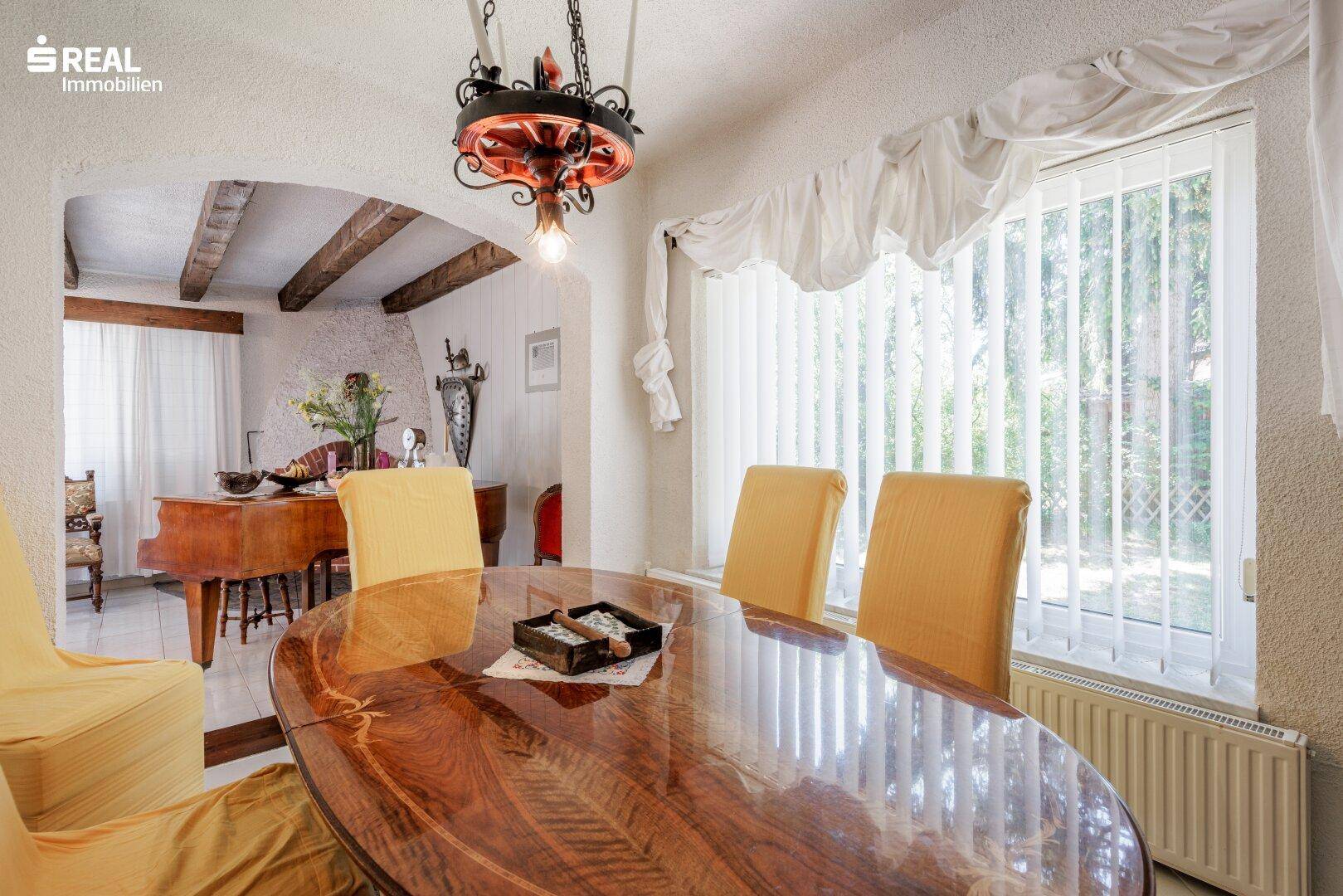 Heller Essbereich mit großem Holztisch, gelben Stühlen und Blick ins Grüne.