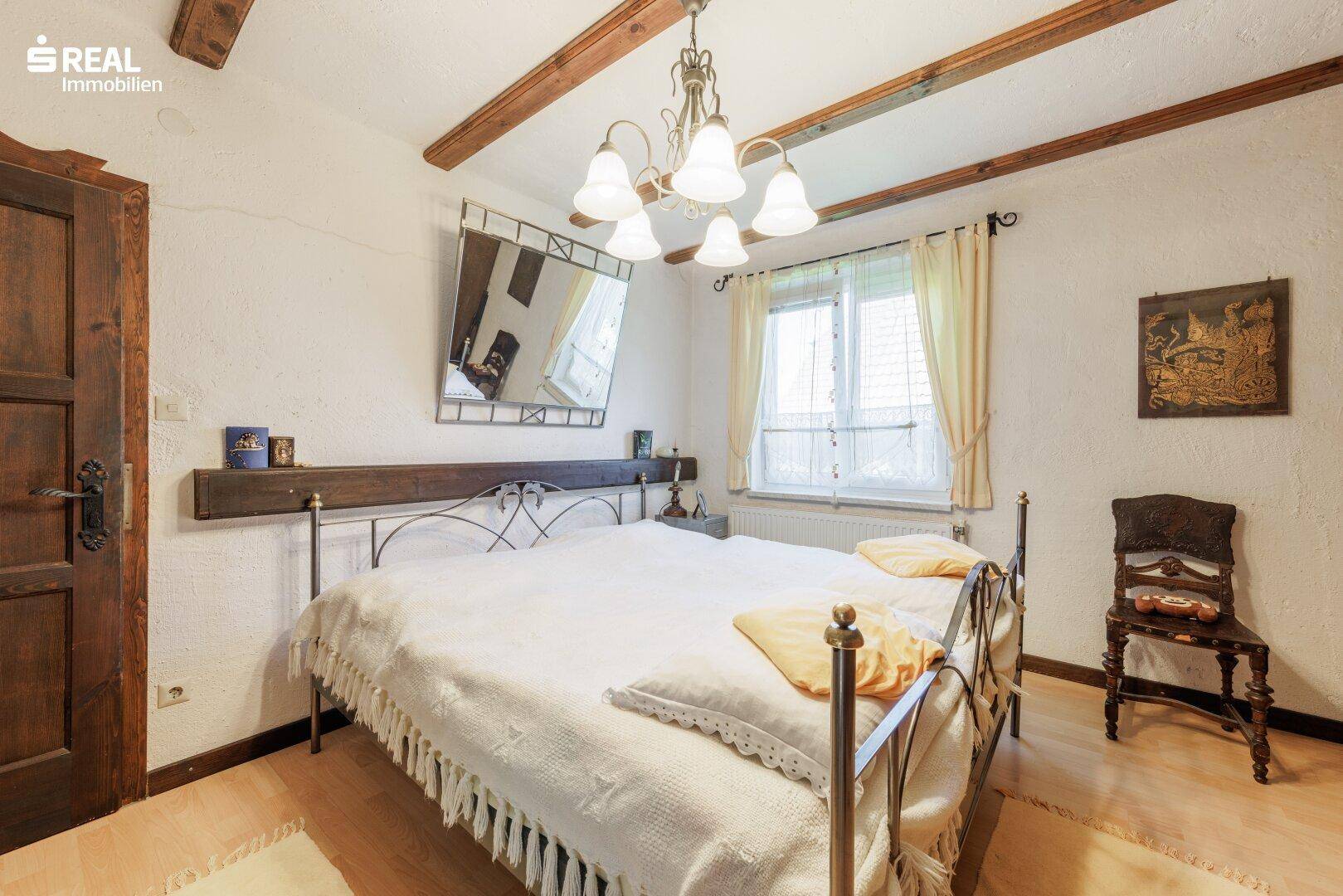 Gemütliches Schlafzimmer mit Doppelbett, Holzbalken und hellem Holzboden.