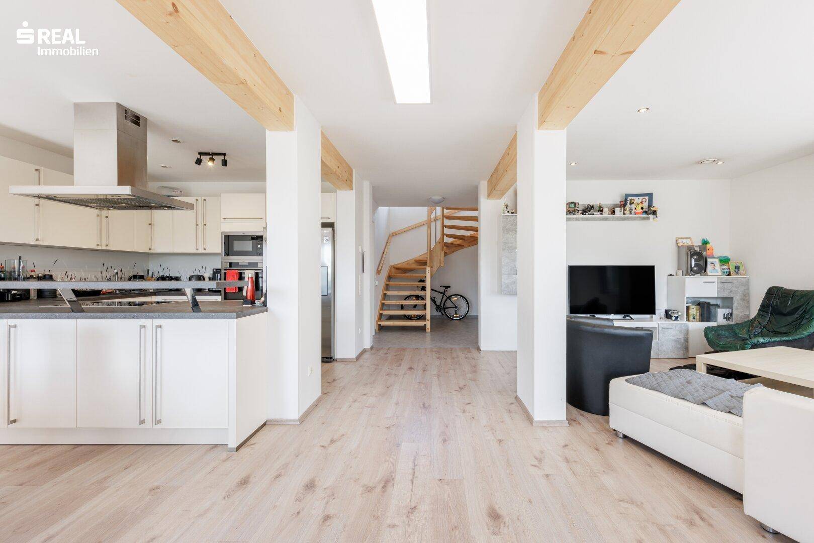 Geräumiger Wohnbereich mit offener Küche, Holzbalken und Treppe zum Obergeschoss.