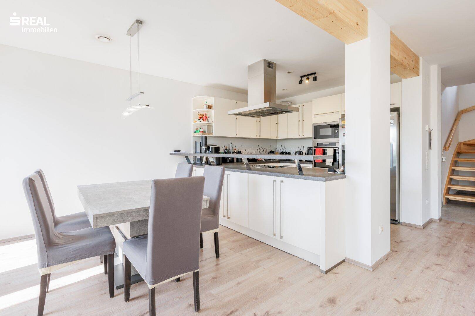 Offene Küche mit Essbereich, weißen Schränken und Holzbalken an der Decke.