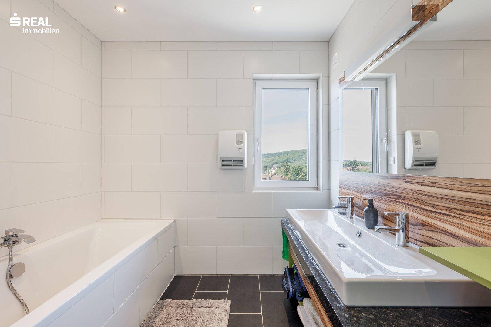 Modernes Badezimmer mit Badewanne, Doppelwaschbecken und Fenster mit Weitblick.