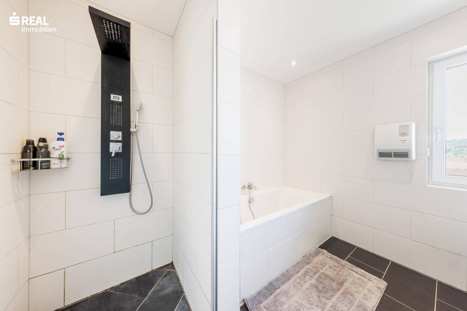 Helles Badezimmer mit Badewanne, moderner Duschkabine und weißen Fliesen.