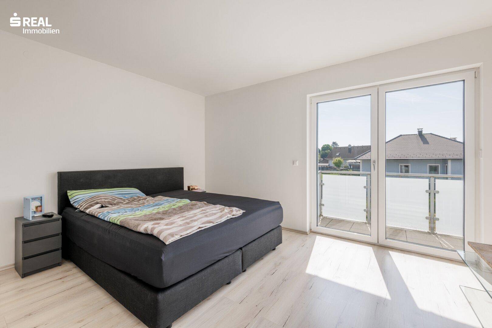 Schlafzimmer mit Doppelbett, hellem Boden und Zugang zum Balkon.