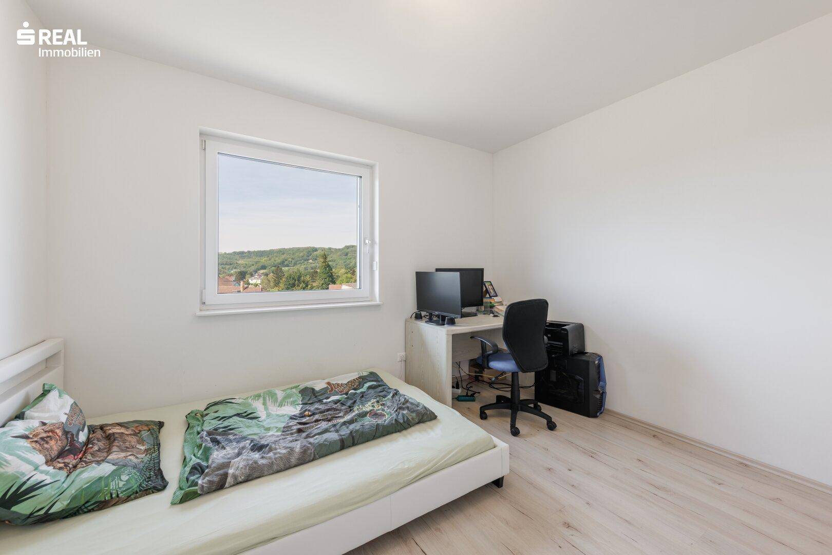 Kinder- oder Gästezimmer mit Bett, Schreibtisch und Blick ins Grüne.