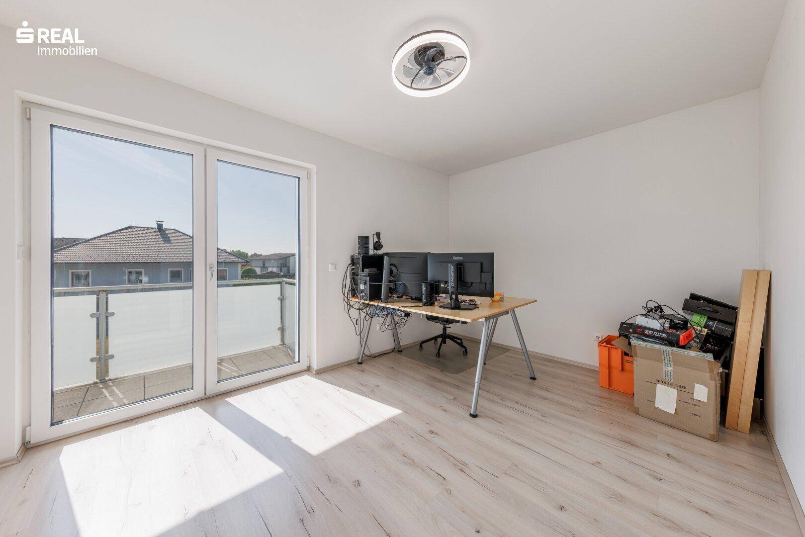 Helles Arbeitszimmer mit Schreibtisch, Computern und Zugang zum Balkon.