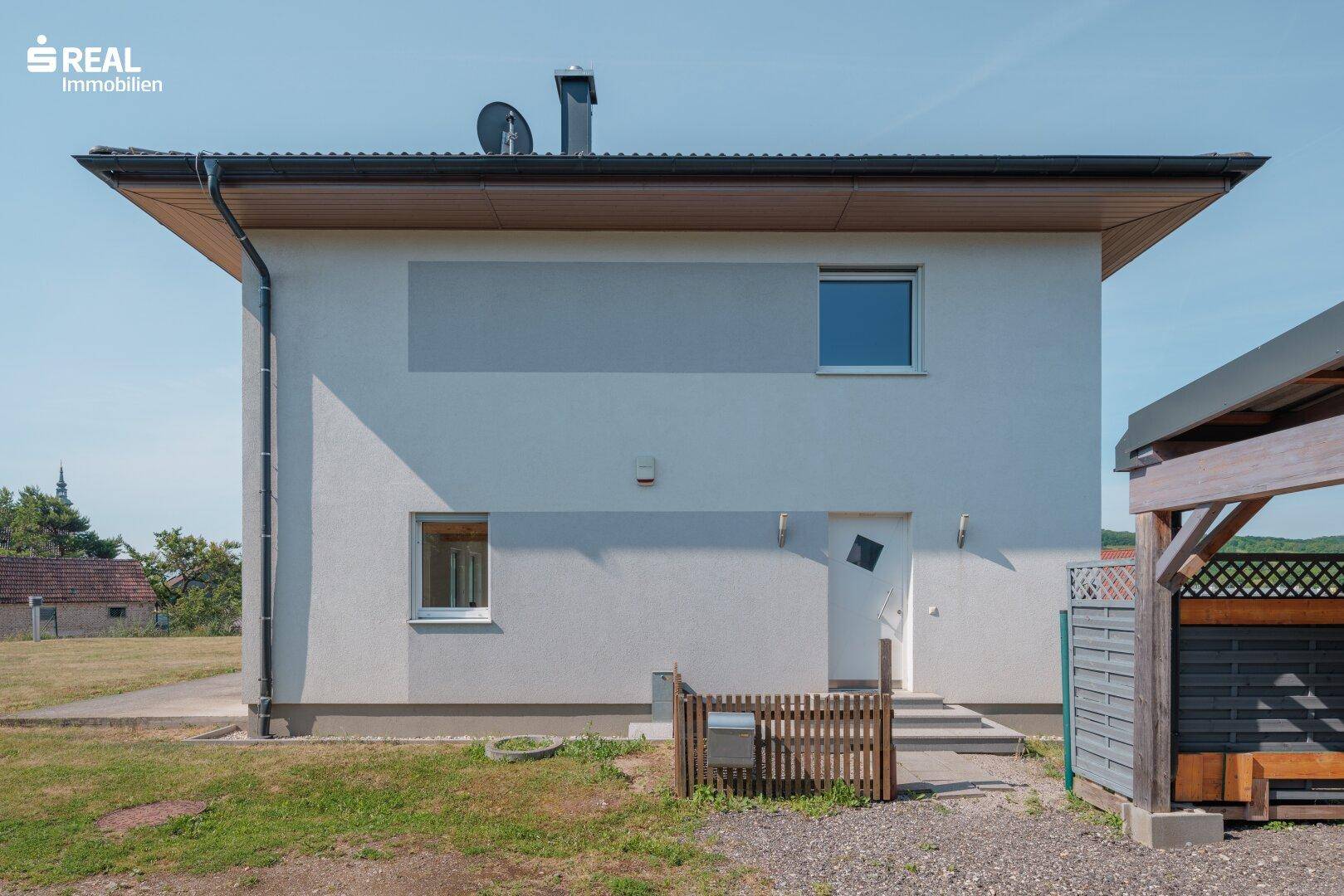 Seitenansicht des Hauses mit Eingangsbereich und Carport im Vordergrund.