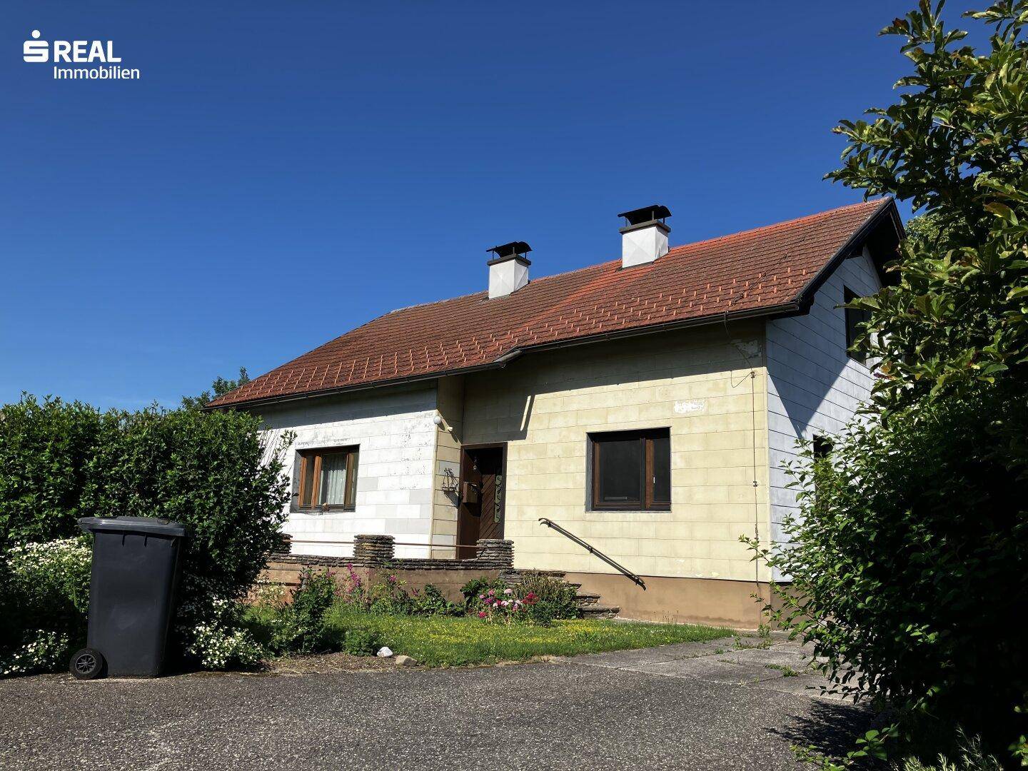 Ansicht des Einfamilienhauses mit Vorgarten, Zufahrt und altem Baumbestand an einem sonnigen Tag.