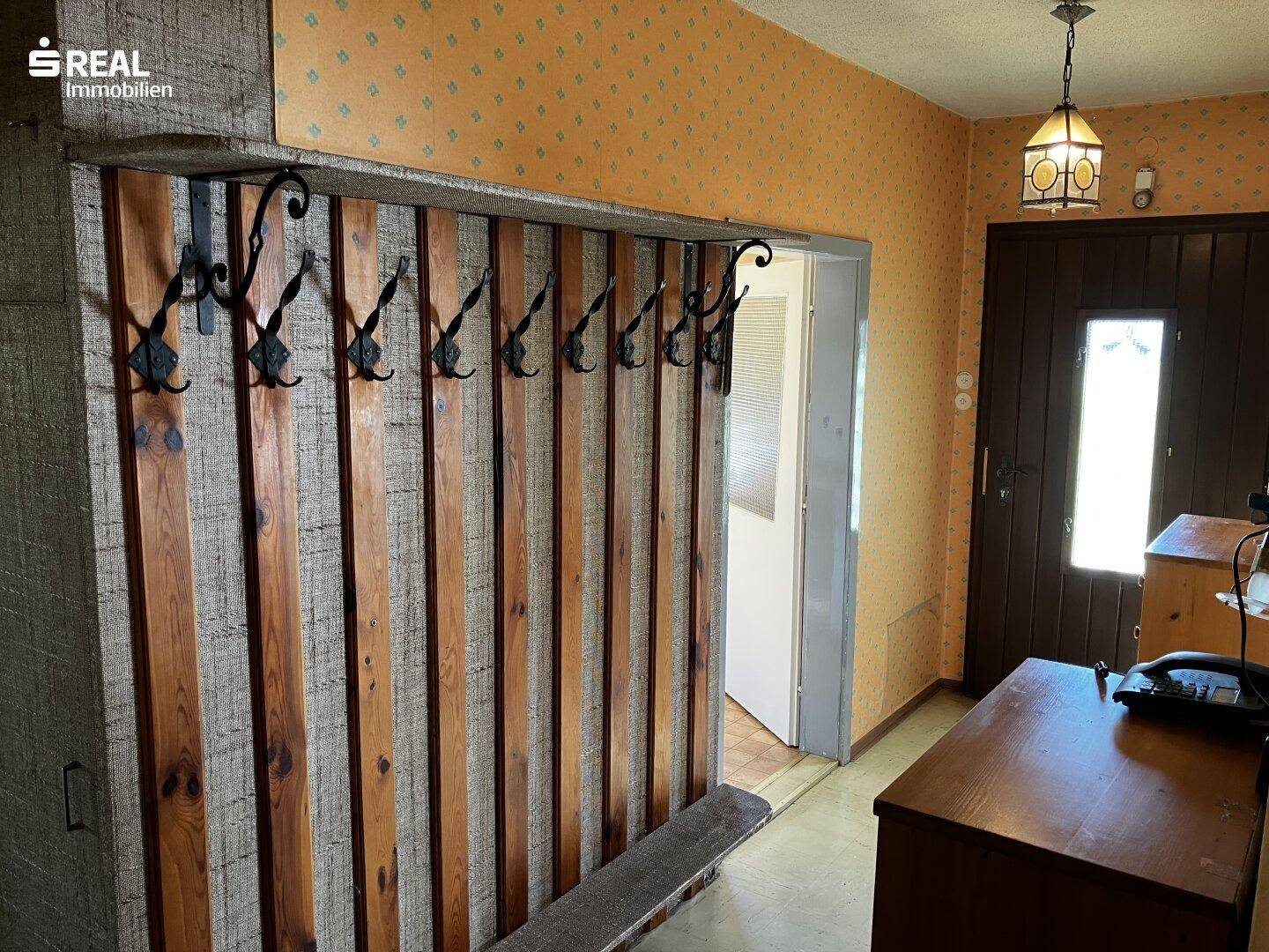 Eingangsbereich mit rustikaler Holzvertäfelung, Garderobe und gemusterter Tapete.
