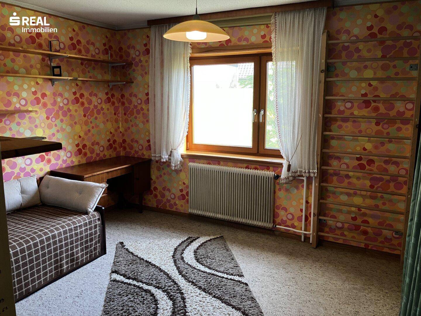 Kinderzimmer oder Gästezimmer mit Teppichboden, Schreibtisch und bunter Tapete.