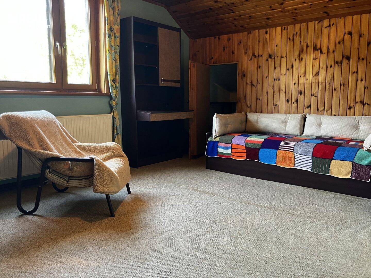 Gemütliches Zimmer mit Holzvertäfelung, Teppichboden und Tagesbett unter Dachschräge.