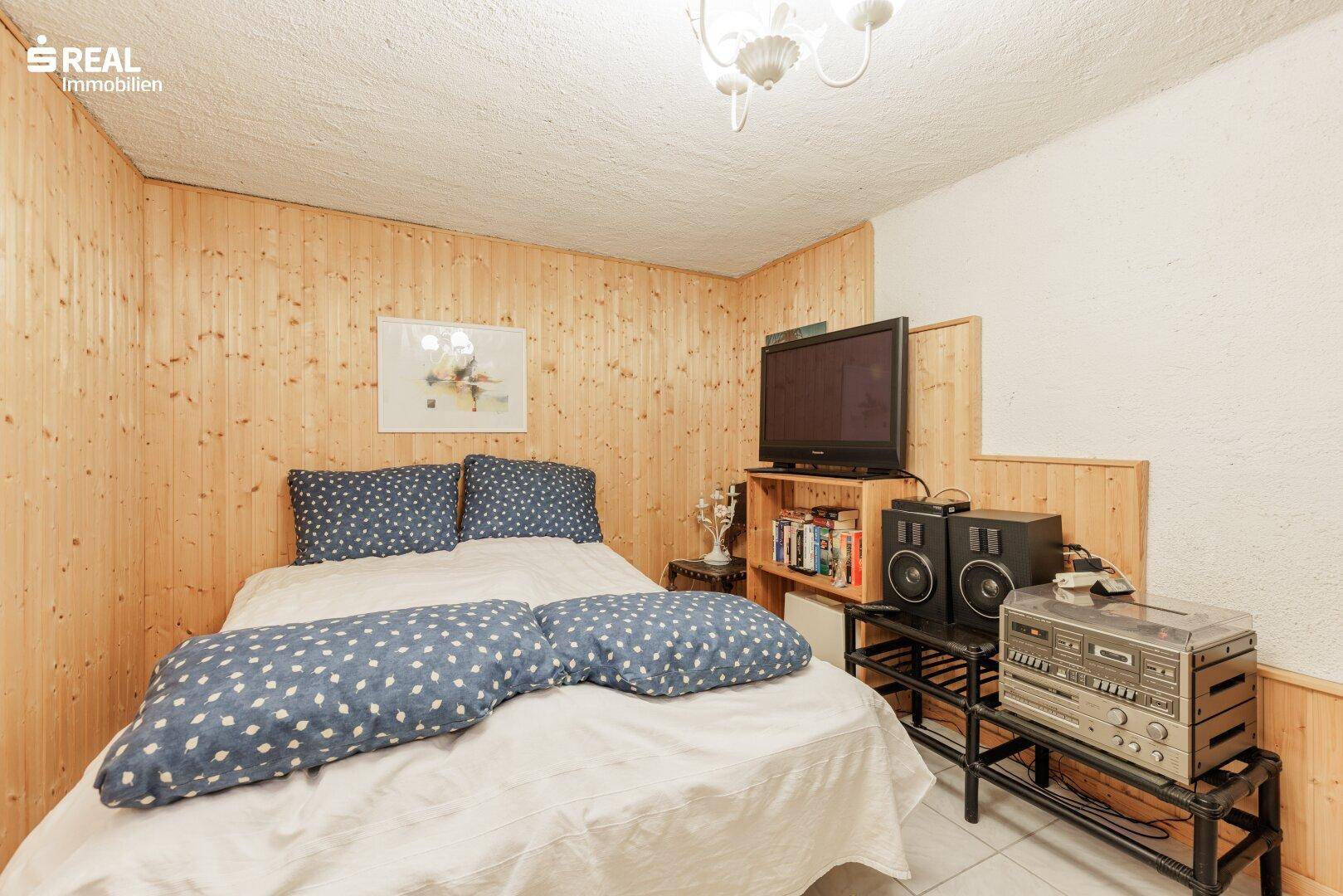 Kellerzimmer mit Bett, Fernseher und Holzvertäfelung, ideal als Gästezimmer.