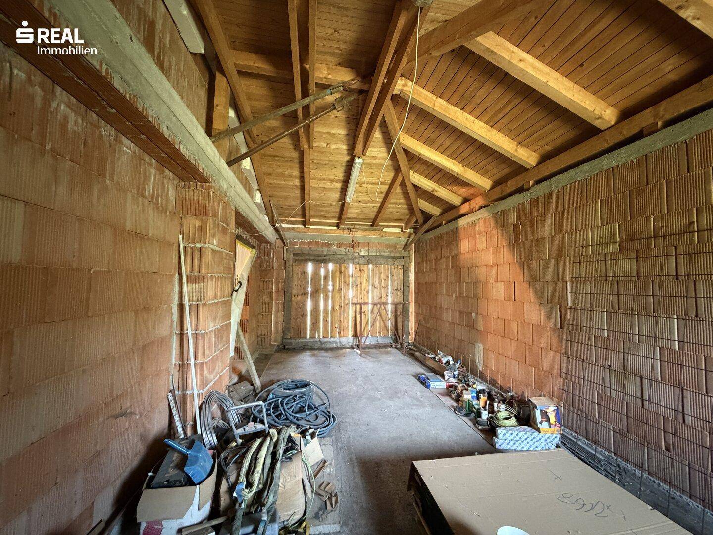 Geräumige Garage im Rohbau mit Holzdachstuhl und Ziegelwänden.