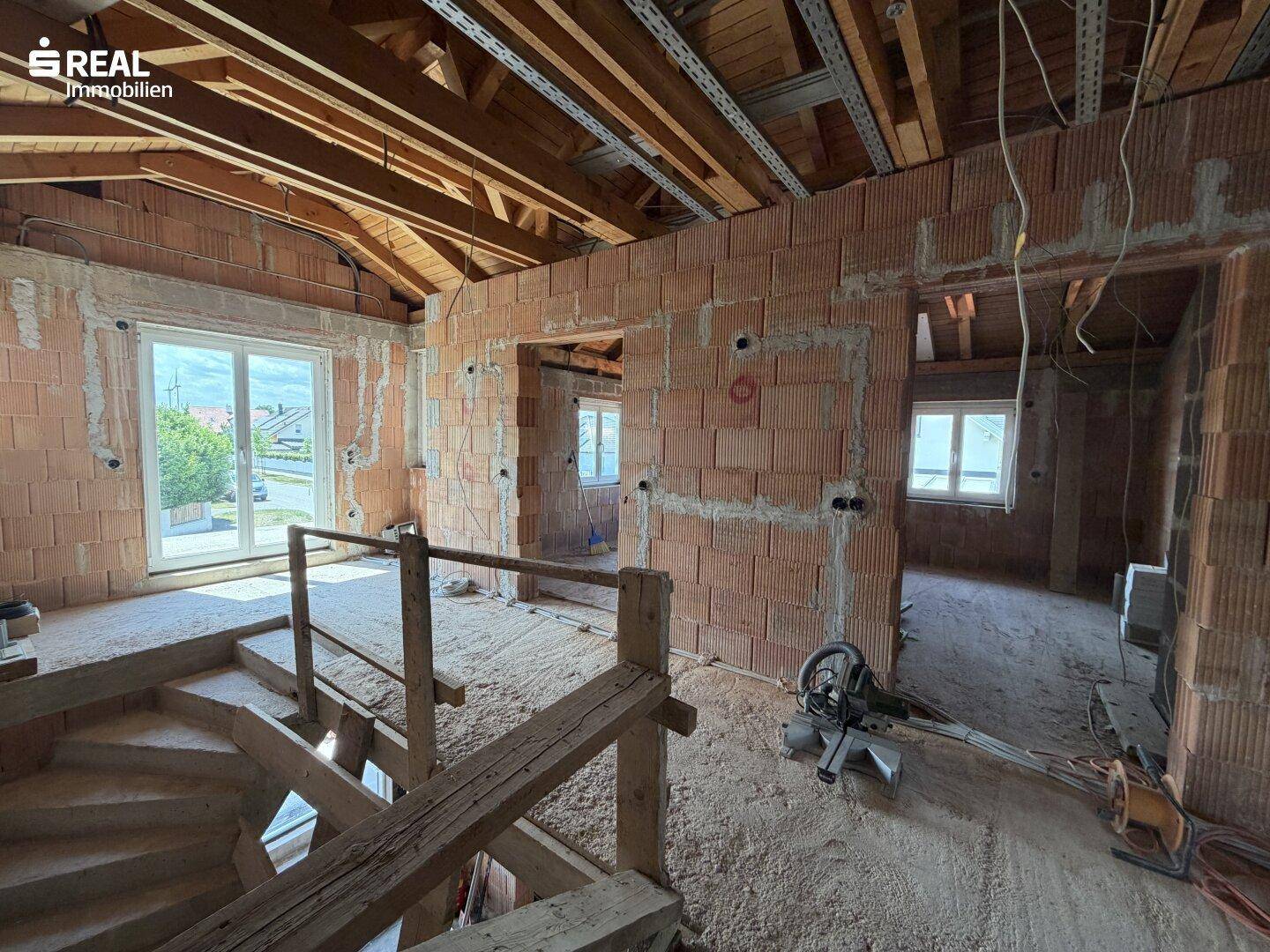 Treppenbereich und Flur im Rohbau mit sichtbaren Holzstrukturen und Ziegelwänden.