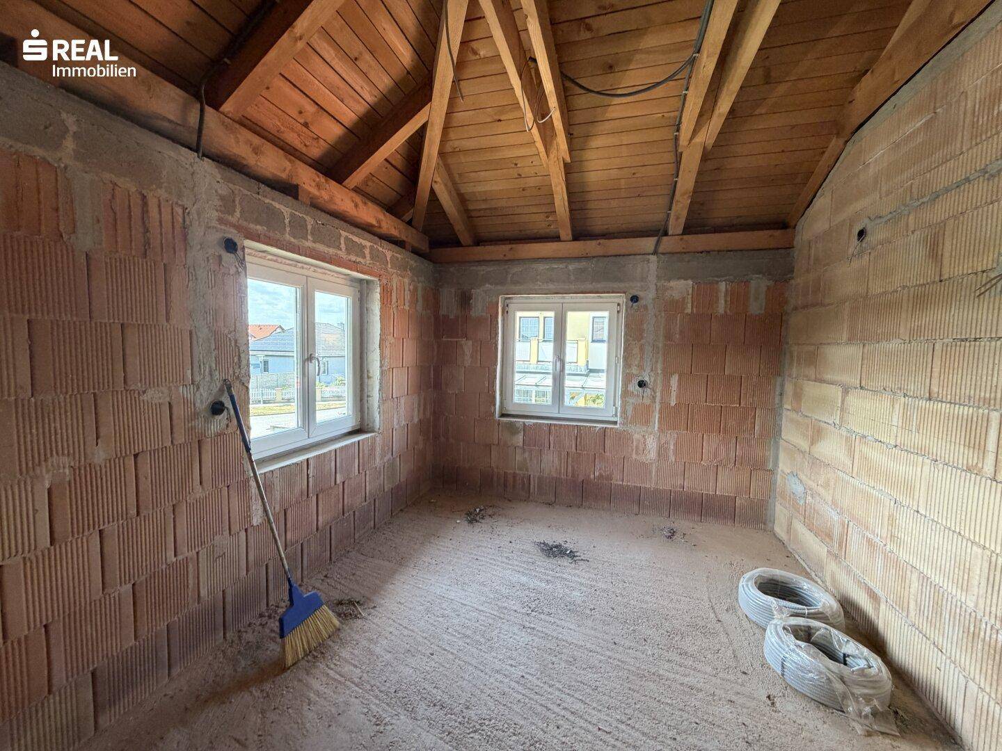 Weiteres Zimmer im Rohbau mit Holzdachstuhl, Ziegelwänden und Blick nach draußen.