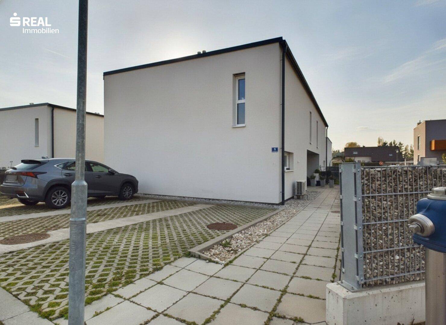 Seitenansicht eines modernen Reihenhauses mit Parkplatz und Kiesbeet.