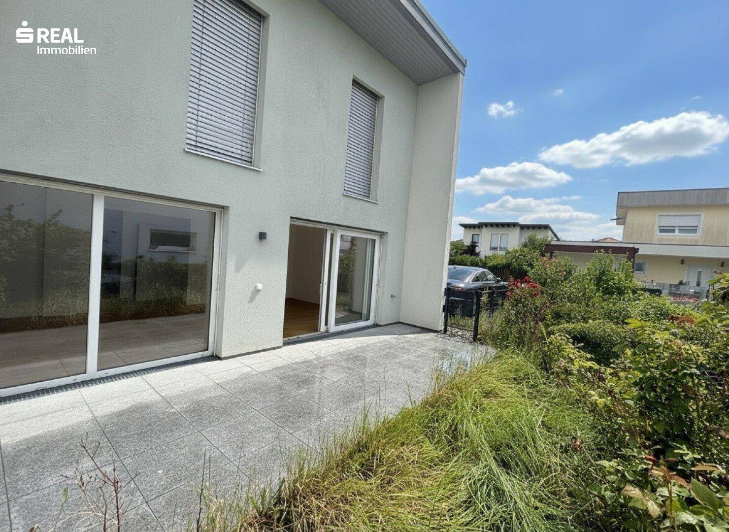 Große, geflieste Terrasse mit Zugang zum Innenbereich und Blick ins Grüne.