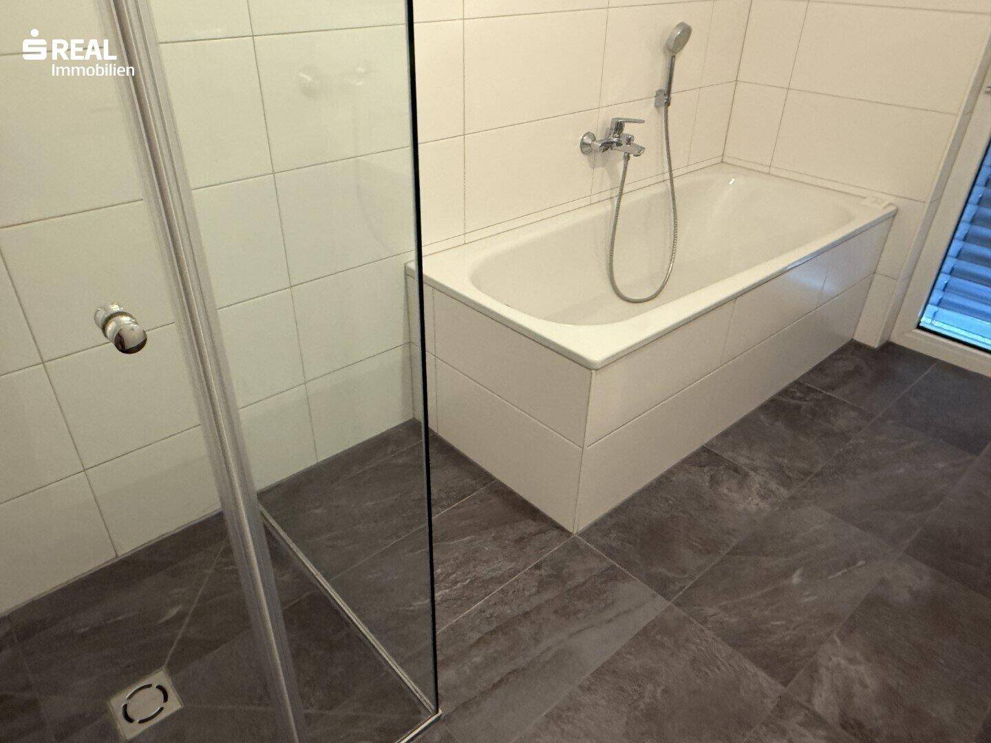 Modernes Badezimmer mit Badewanne und separater Duschkabine, komplett gefliest.