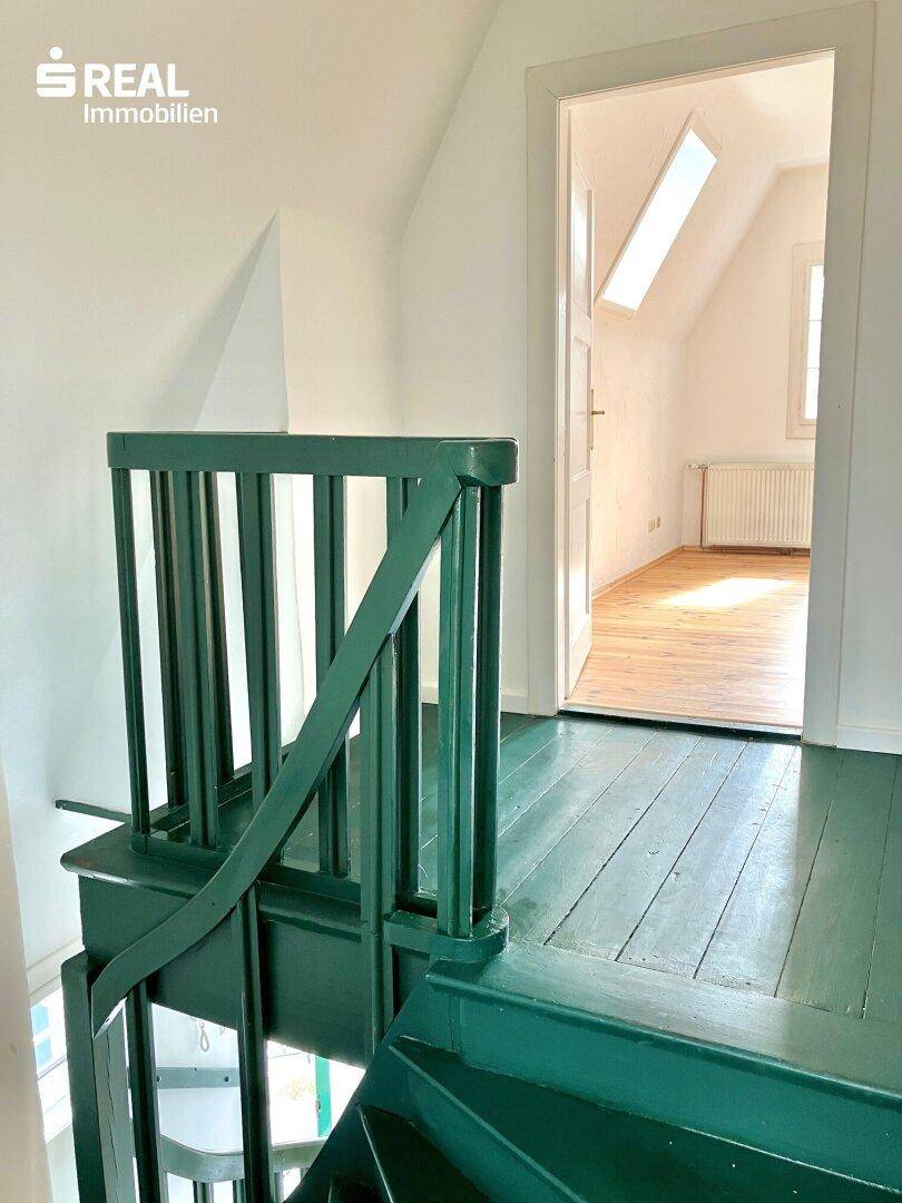 Treppenhaus mit grün gestrichenen Holzstufen und Geländer, das zu einem hellen Zimmer führt.