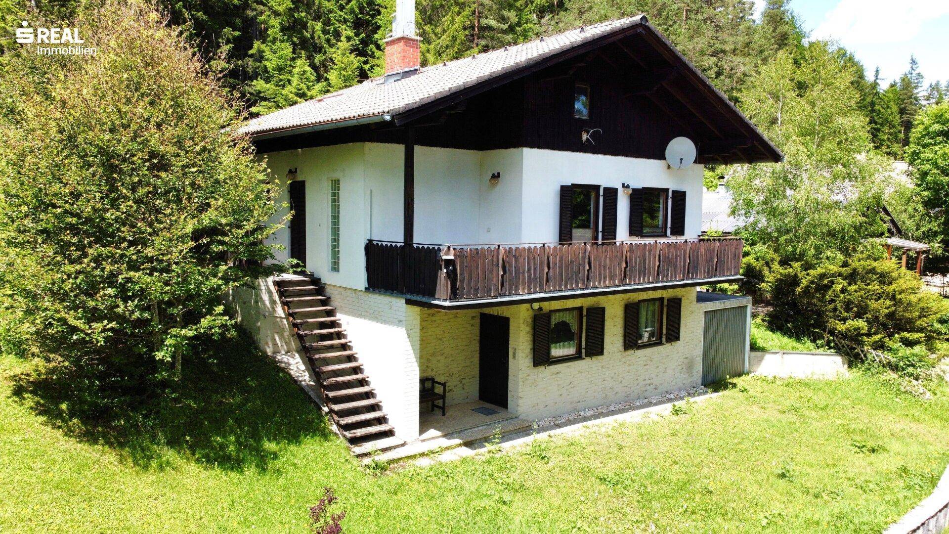 Traditionelles Haus mit Balkon und Außentreppe, umgeben von viel Grün und Wald.