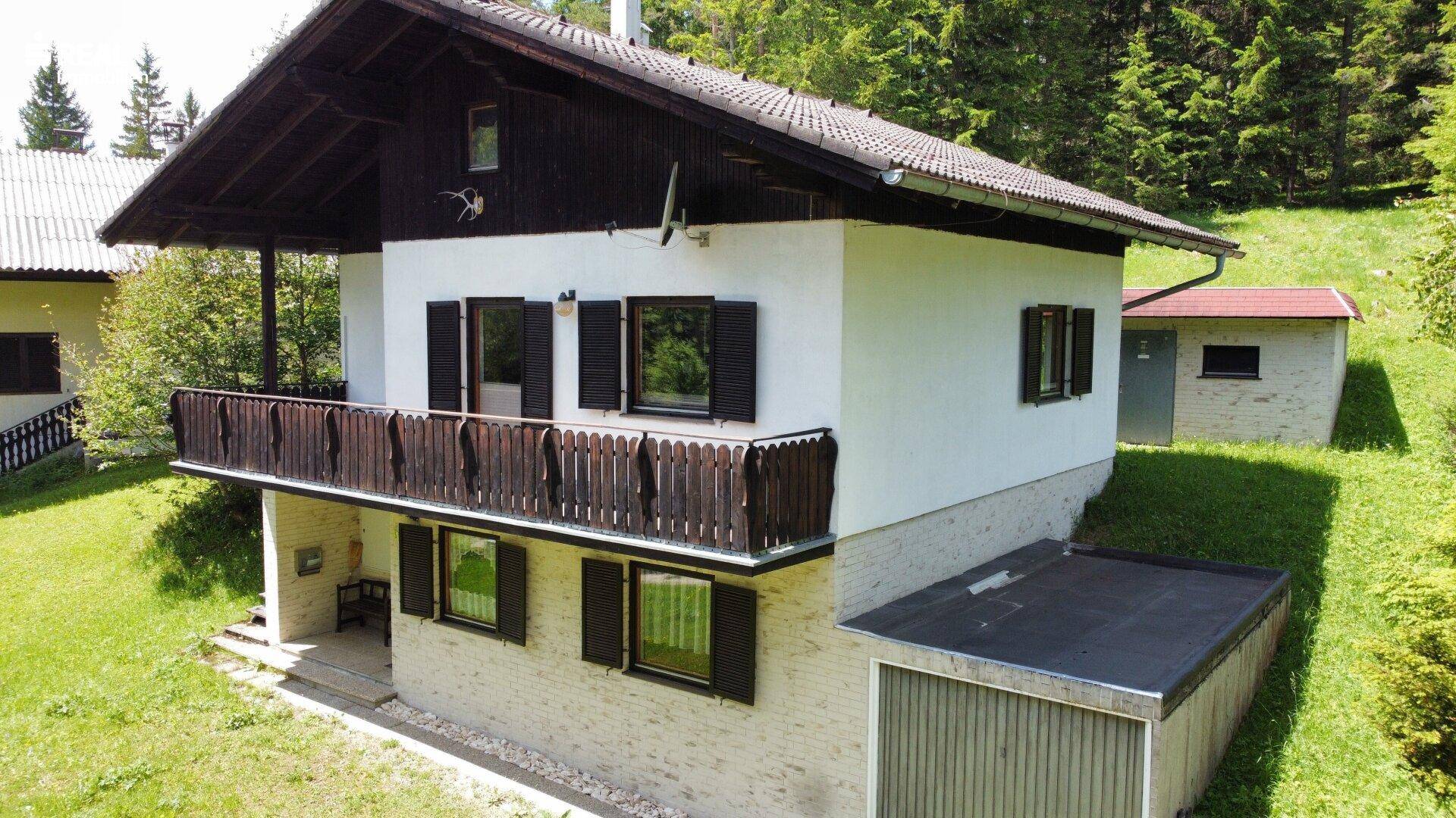 Freistehendes Haus mit Balkon und angrenzendem Nebengebäude in ländlicher Umgebung.