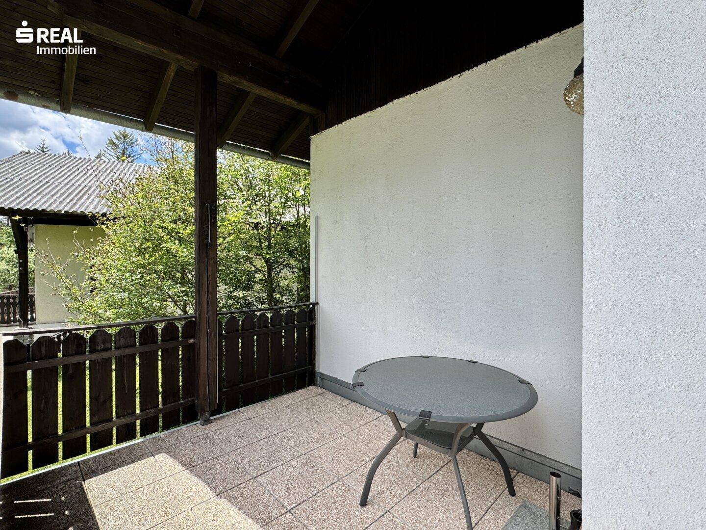 Überdachter Balkon mit kleinem Tisch, ideal für entspannte Stunden im Freien mit Blick ins Grüne.