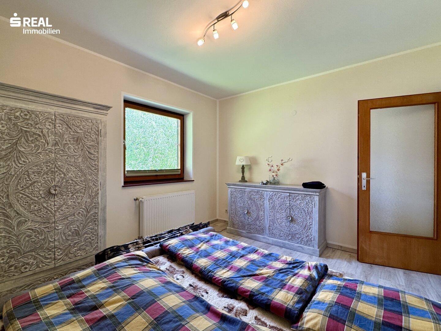 Schlafzimmer mit hellem Laminatboden und kunstvoll geschnitzten Holzmöbeln.