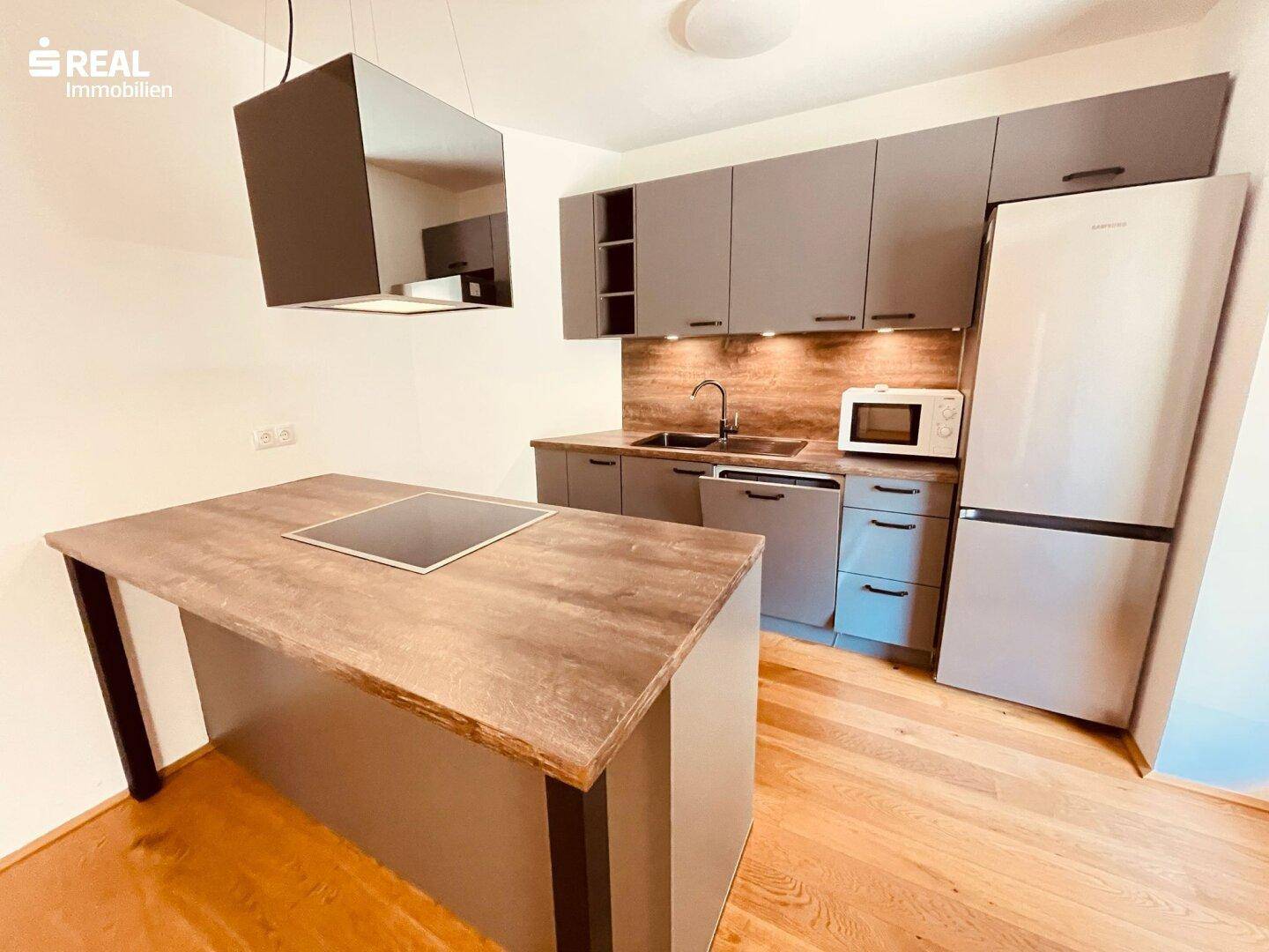 Moderne Einbauküche mit grauen Fronten, Induktionskochfeld auf der Insel und integrierten Geräten.