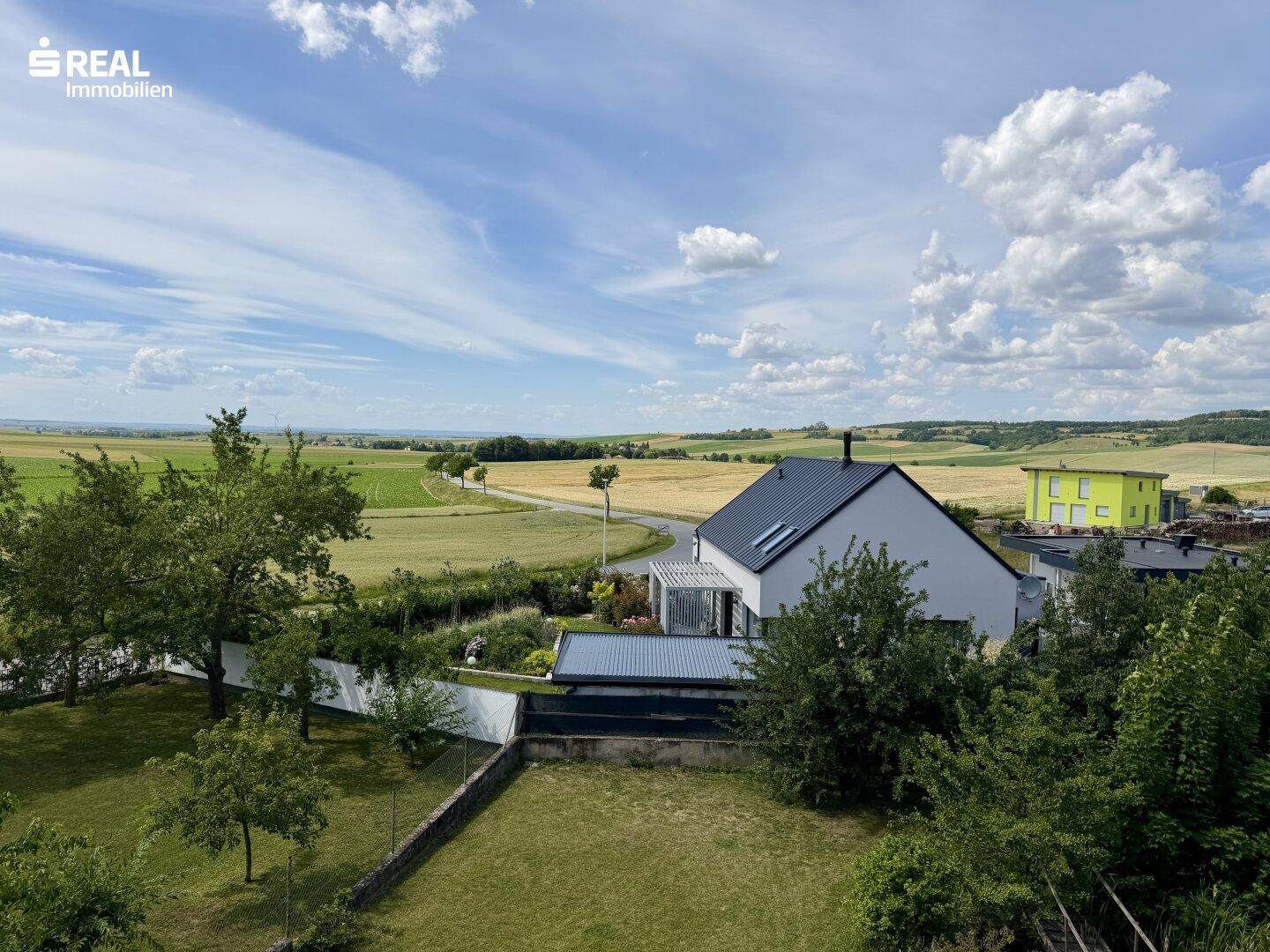 Weitläufiger Blick über die ländliche Umgebung mit Feldern, Bäumen und einem weiteren Haus.