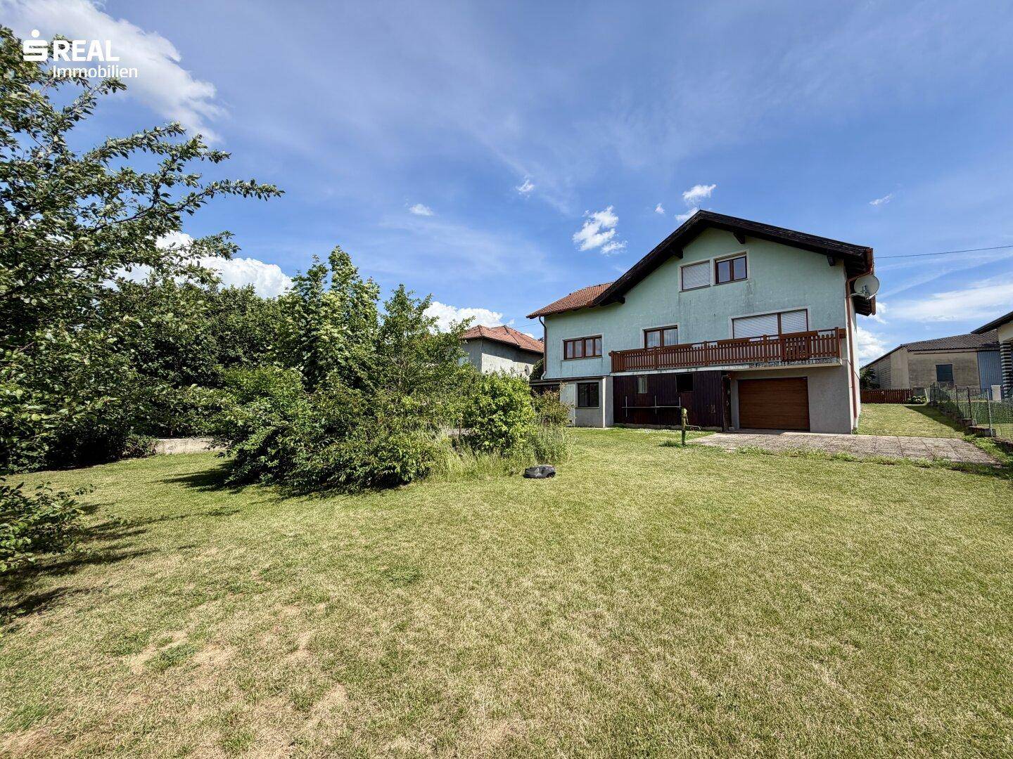 Rückansicht des Hauses mit großem Garten, Bäumen und einer Garage im Erdgeschoss.