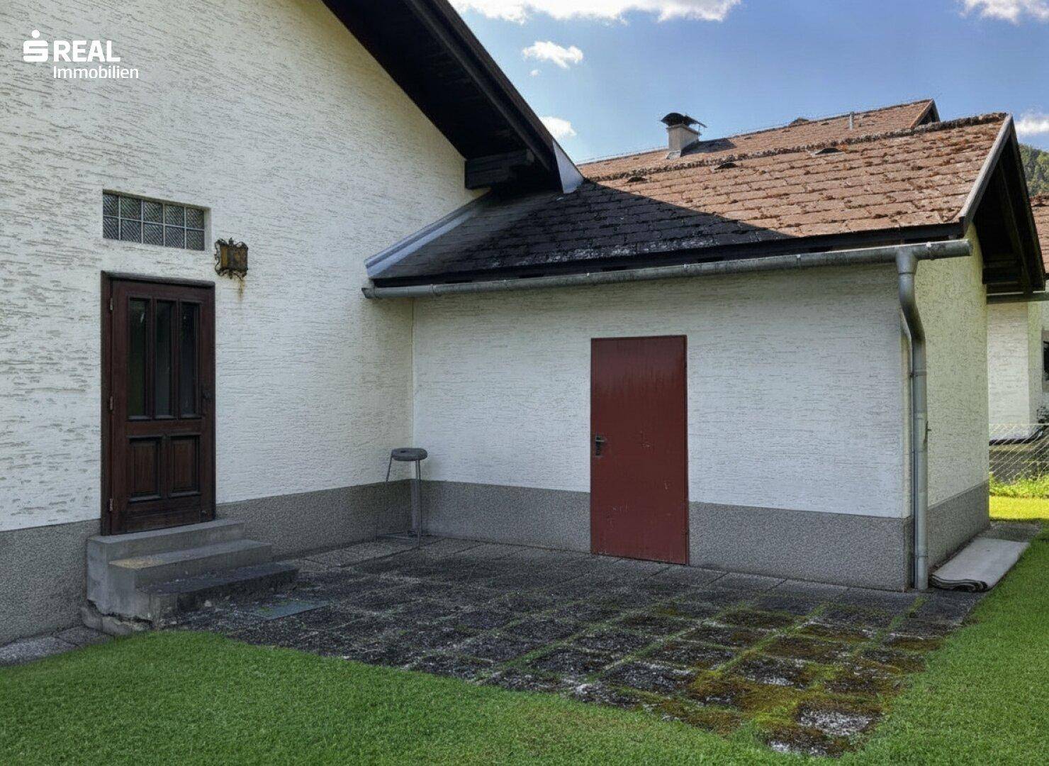 Hinterer Eingangsbereich mit gepflasterter Terrasse und Zugang zu einem Nebengebäude.