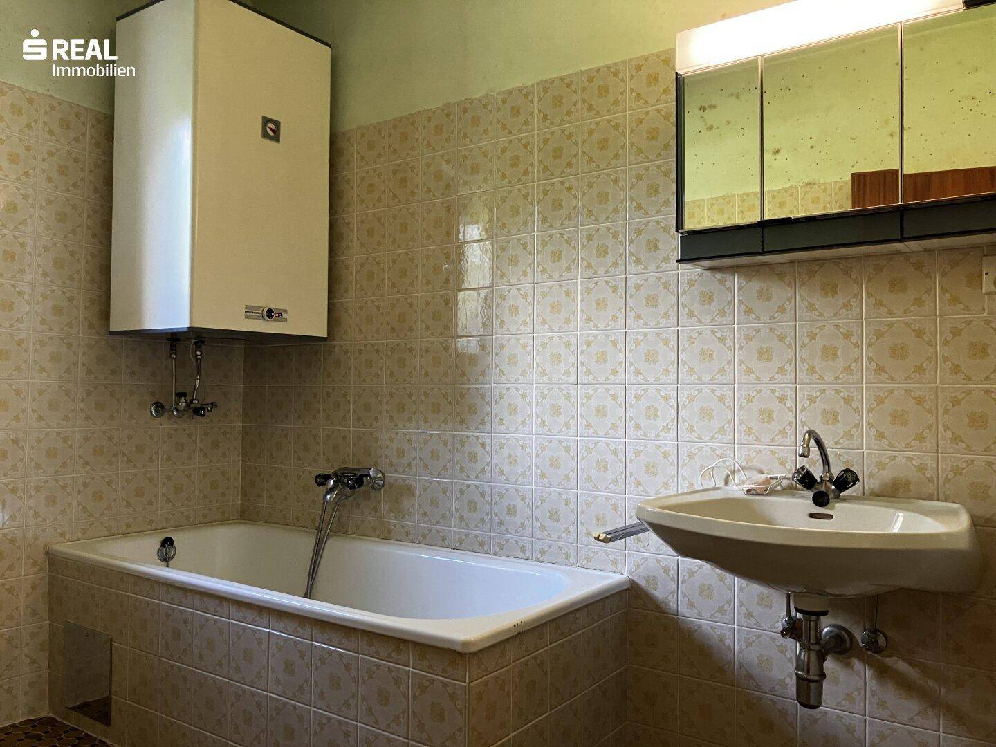 Badezimmer mit Badewanne, Waschbecken und Wandfliesen im Stil der 80er Jahre.
